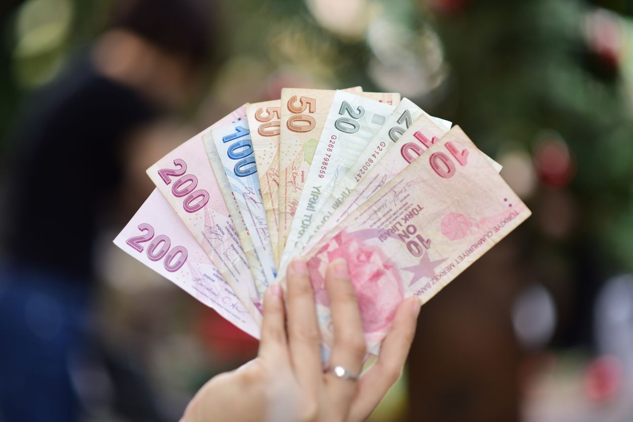 Services Hand holding multiple denominations of Turkish Lira banknotes outdoors.
